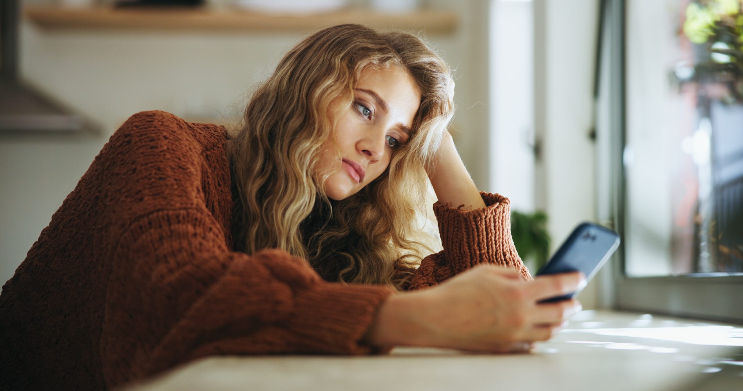 Junge Frau blickt unzufrieden auf ihr Smartphone, unter Druck durch Social-Media-Schönheitsideale.